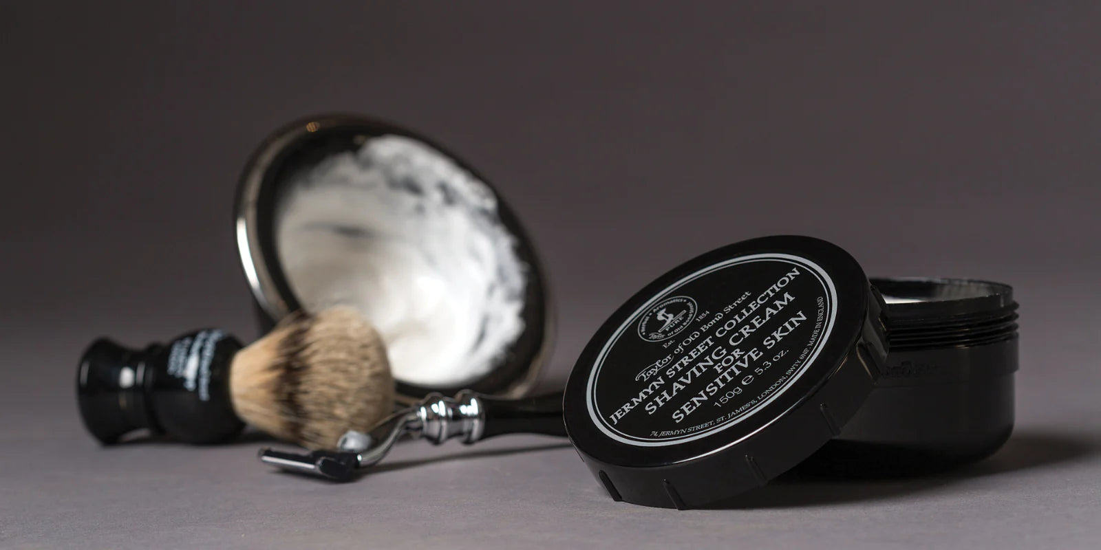 Grooming essentials including shaving cream, brush, and bowl on a grey background.