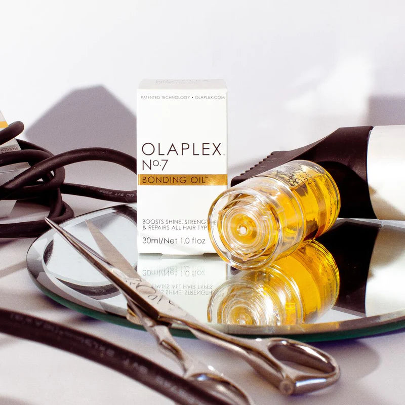 Olaplex No. 7 Bonding Oil bottle with scissors and mirror, haircare product for boosting shine and repairing damaged hair.