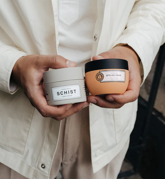 Person holding premium hair styling and fiber cream products in stylish containers.