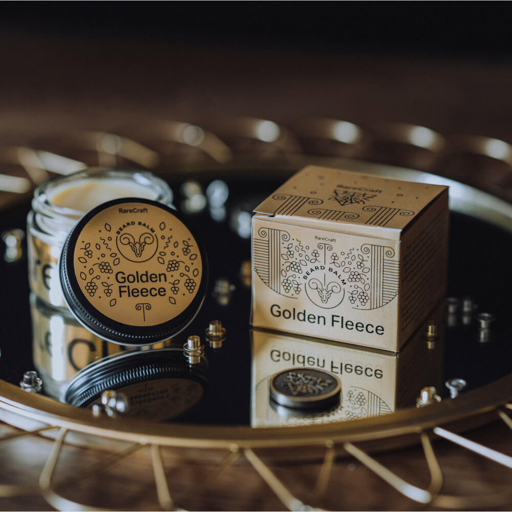 Golden Fleece hair and beard balm in a decorative tin, displayed with its matching box on a reflective surface.